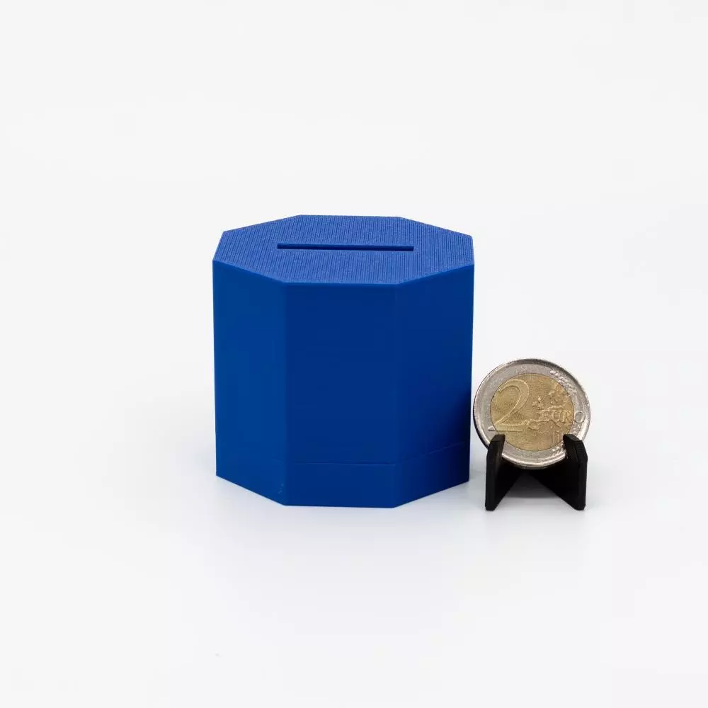 Geschlossene marineblaue flache oktagonale PAZL Box Athene mit Münzschlitz neben 2-Euro-Münze – Größenvergleich, Box breiter und flacher