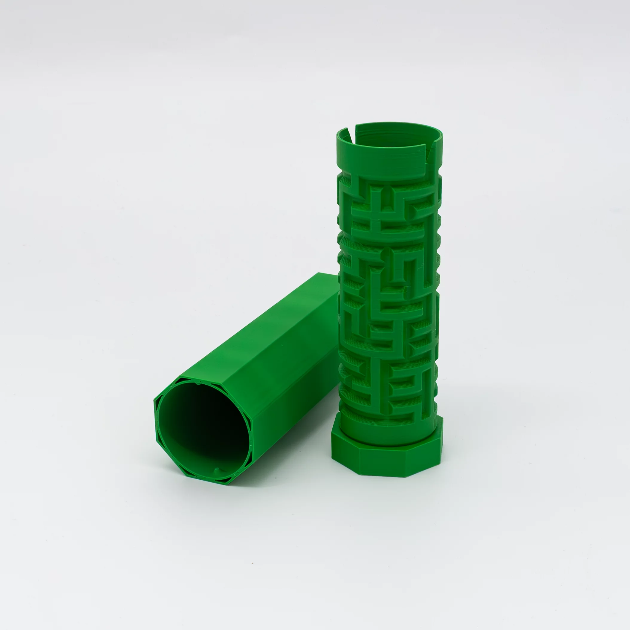 Two green cylinders, one standing with a raised labyrinth pattern, the other lying flat and smooth. Both 3D-printed with octagonal openings, shown on a white background.