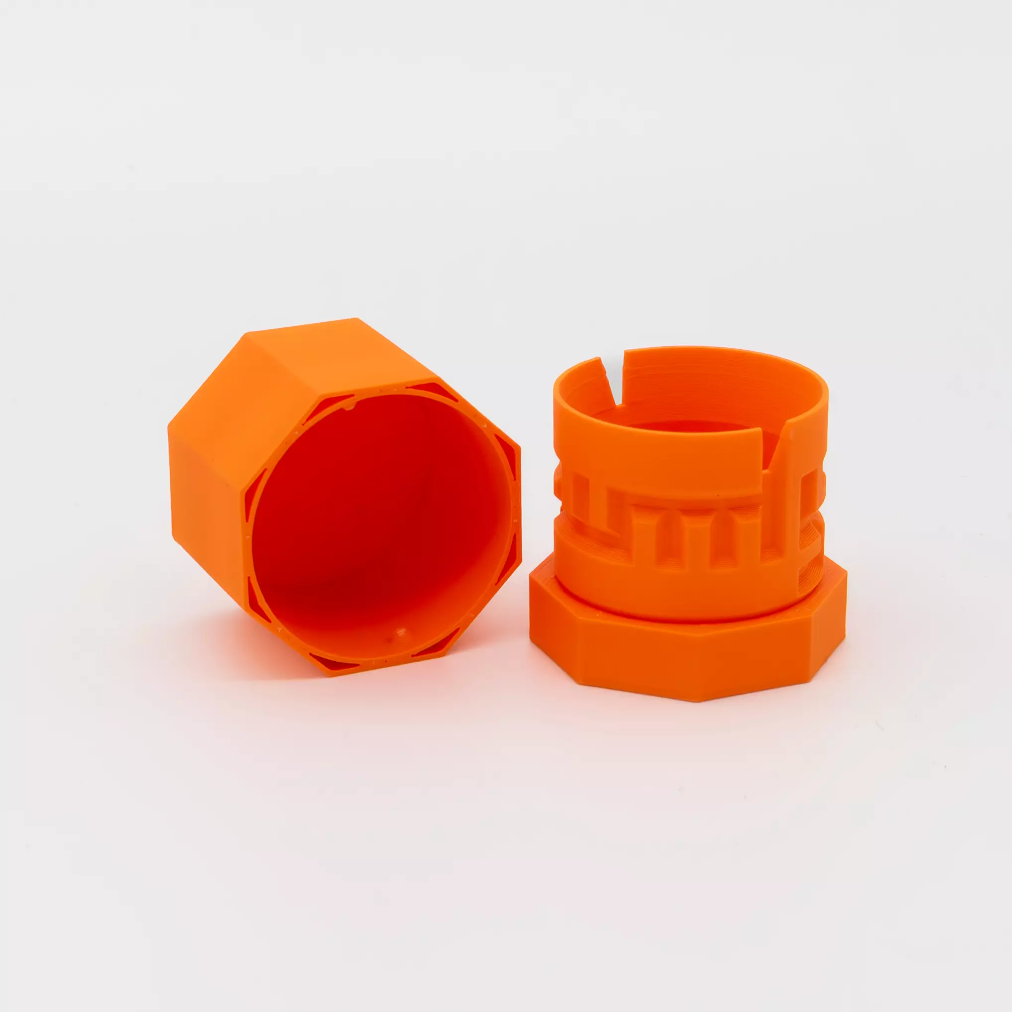 Two short orange cylinders made with a 3D printer. One has a smooth surface, the other features a labyrinth pattern. Both are shown against a white background.