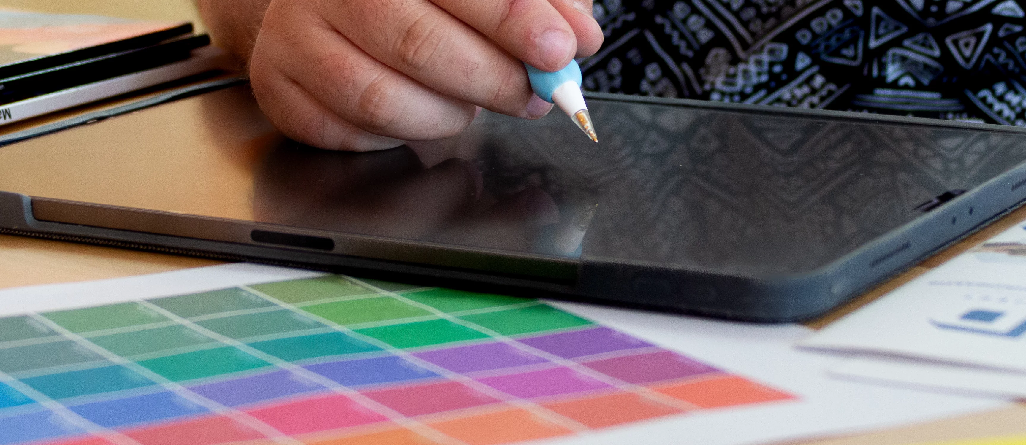 A hand holds a white stylus above a black tablet. Below are rainbow-colored swatches. A snapshot from a creative design process.